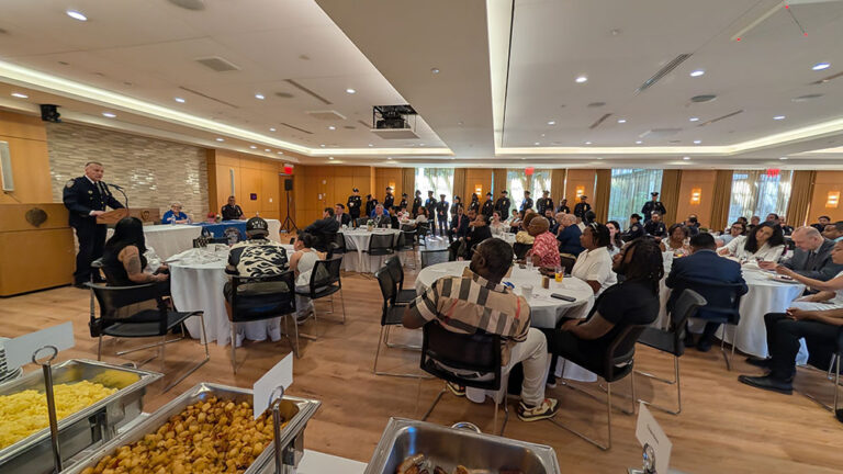 Attendees sitting at tables listening to a speaker at the podium