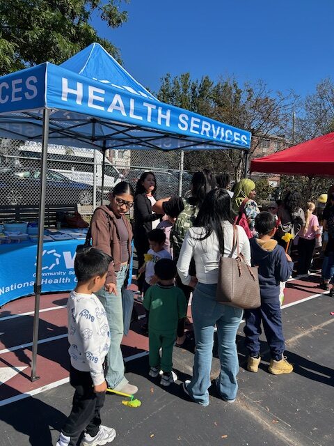 Attendees in front of VIP Community Services' Health Services table and tent at the Fruit & Vegetable Distribution.